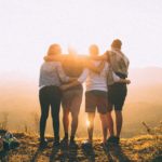 Vier vrienden arm in arm kijken samen naar de ondergaande zon.