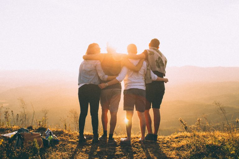 Vier vrienden arm in arm kijken samen naar de ondergaande zon.
