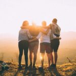 Vier vrienden arm in arm kijken samen naar de ondergaande zon.