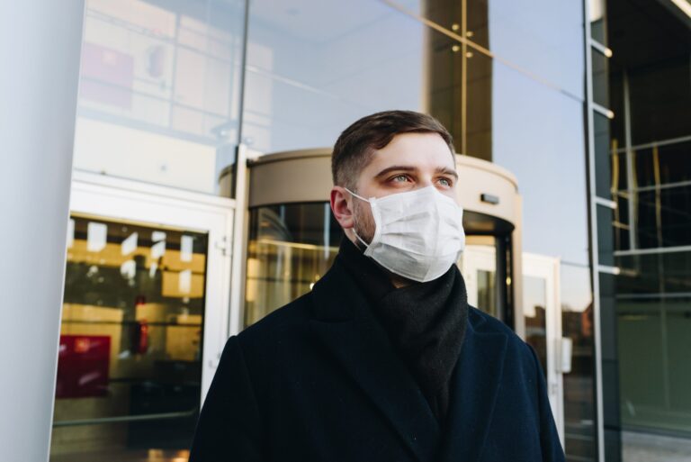 Man, jonge professional, buiten zijn kantoor tijdens de uitbraak en pandemie van het coronavirus COVID-19, draagt een gezichtsmasker.