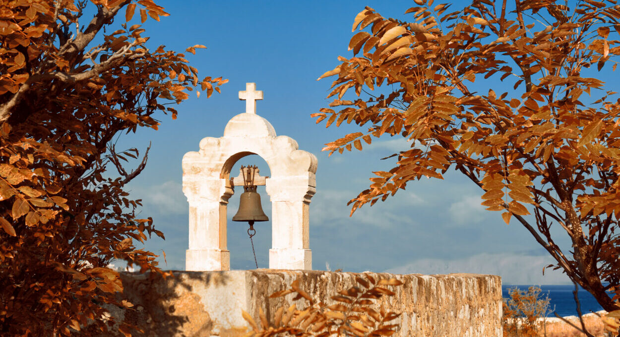 Middeleeuwse klokkentoren met een bronzen bel, omringd door oranje herfstbladeren, met uitzicht op zee bij Rethymnon, Kreta.