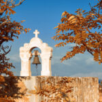 Middeleeuwse klokkentoren met een bronzen bel, omringd door oranje herfstbladeren, met uitzicht op zee bij Rethymnon, Kreta.