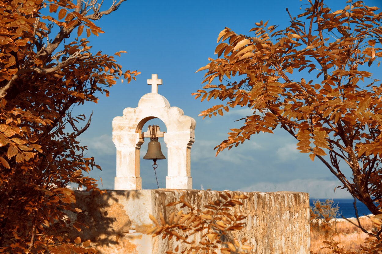 Middeleeuwse klokkentoren met een bronzen bel, omringd door oranje herfstbladeren, met uitzicht op zee bij Rethymnon, Kreta.