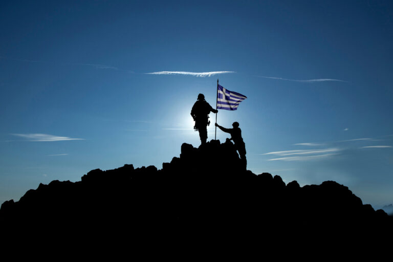 Silhouet van Griekse militairen met de Griekse vlag op een bergtop bij zonsondergang